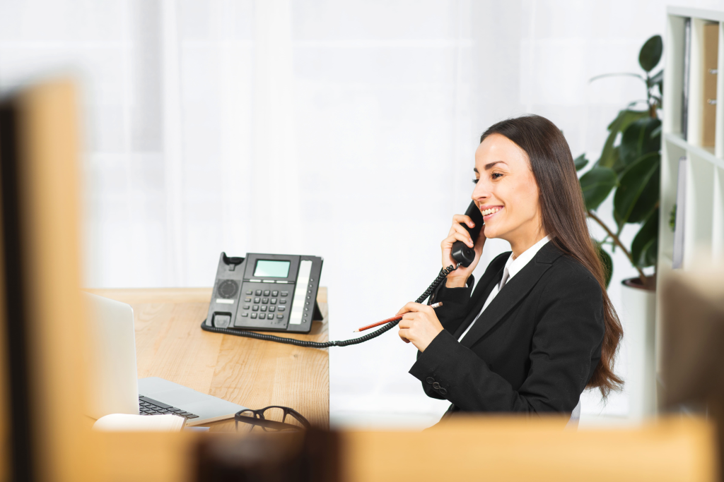 Happy young woman talking on the office phone and smiling while sitting at her working place in office